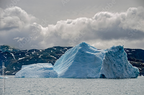 Iceberg with a mountainous and cloudy background
