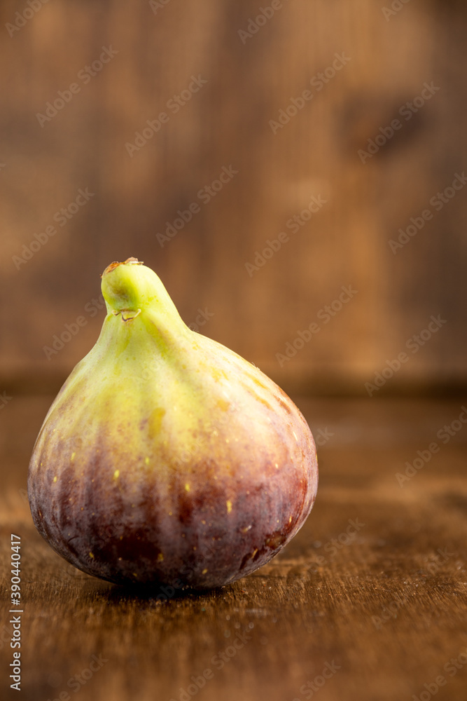 Obraz premium Close-up of a fig, on table and defocused wooden background, vertically, with copy space