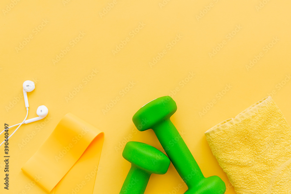 Green dumbbells, towel and headphones on yellow background. Female fitness, home workout concept. Place for text. Green dumbbells, towel and headphones on yellow background. Female fitness, home workout concept. Place for text.