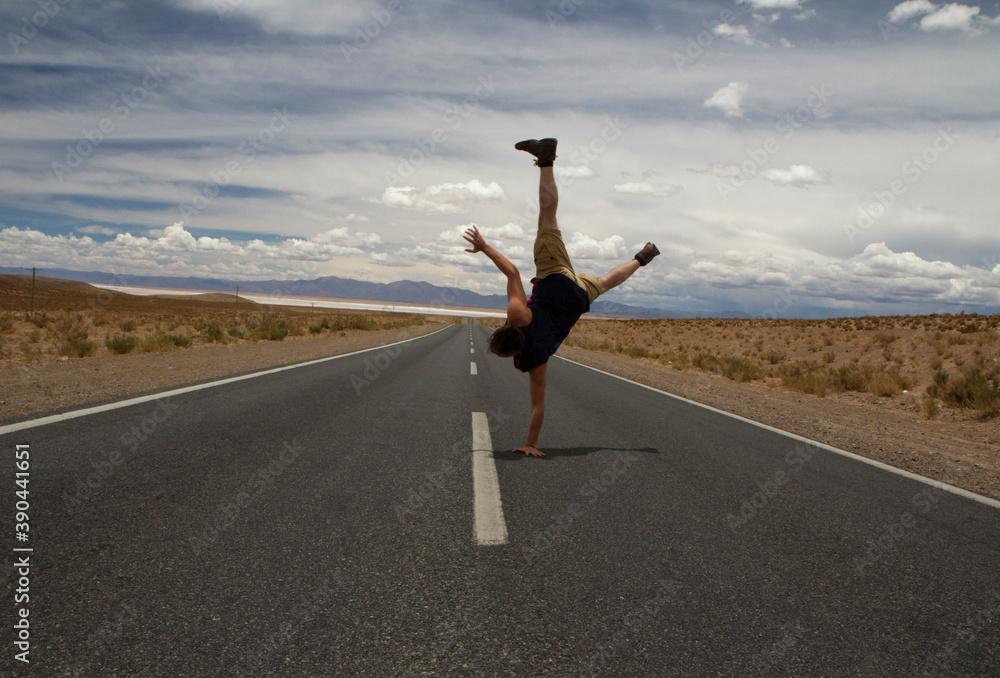 Obraz premium Young caucasian man breakdance move. Handstand in the asphalt desert road. 