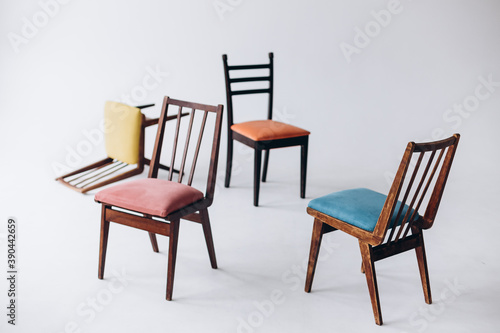 Four old wooden chairs with different colored seats stand empty on a white background  one chair inverted  selective focus