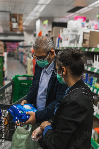 A Caucasian couple shopping at the supermarket during the Covid-19 pandemic. Both are wearing a mask to protect themselves from infection. Their age is about 50 years.