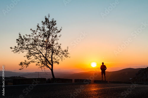 Silhouette of a person standing by a tree looking at the sunrise