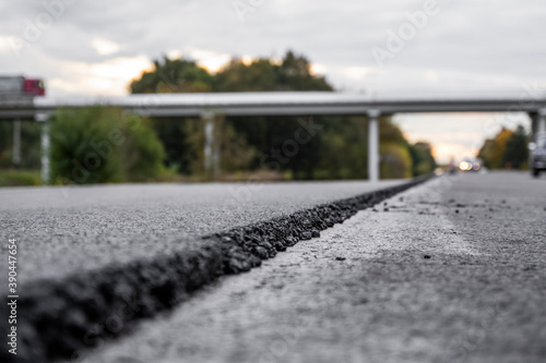 A large layer of fresh hot asphalt. Layer of asphalt raw material in a shallow depth of field. Rollers rollin fresh hot asphalt on the new road. Road construction. Construction of a new road.