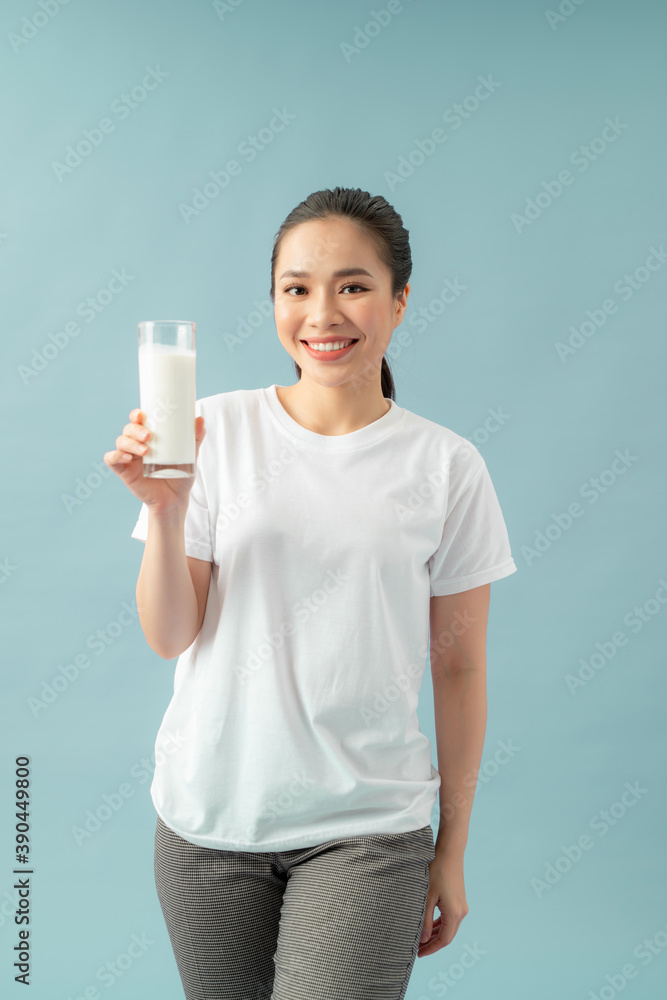 Smiling woman holding a glass of milk against a blue background Smiling woman holding a glass of milk against a blue background