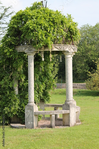 Decorative marble stone garden arbour with green foliage growing over it