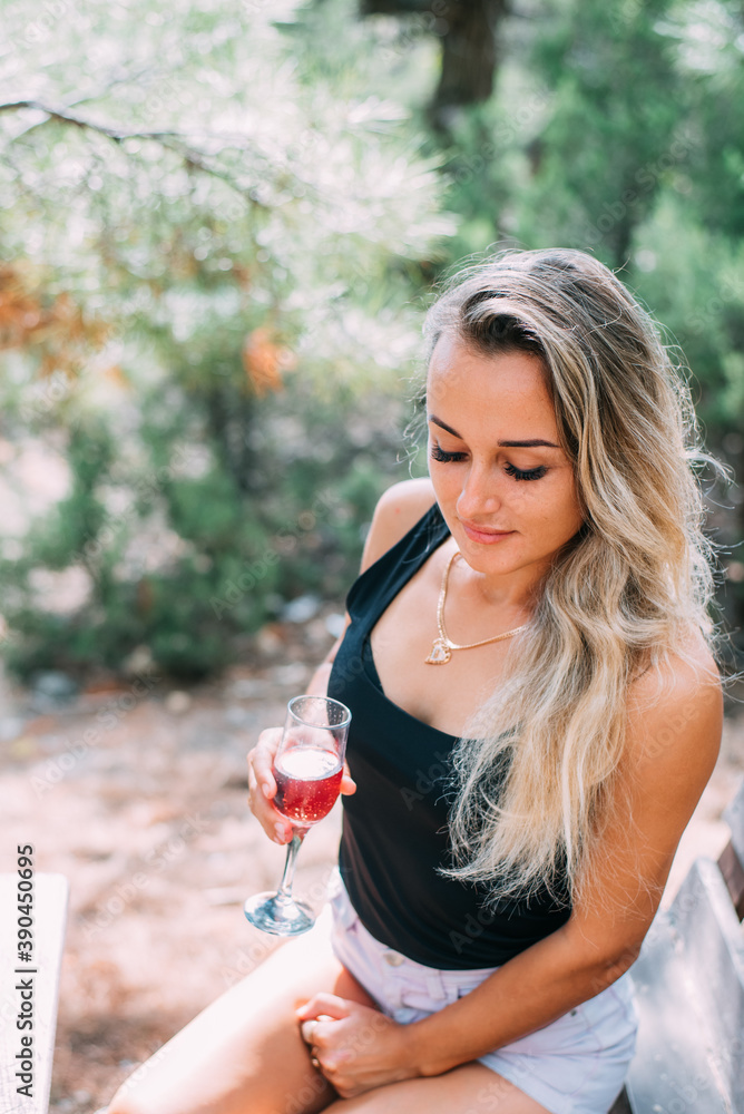 A beautiful girl in a juniper and pine forest with a glass of champagne or wine sits on a wooden pallet, during the day A beautiful girl in a juniper and pine forest with a glass of champagne or wine sits on a wooden pallet, during the day