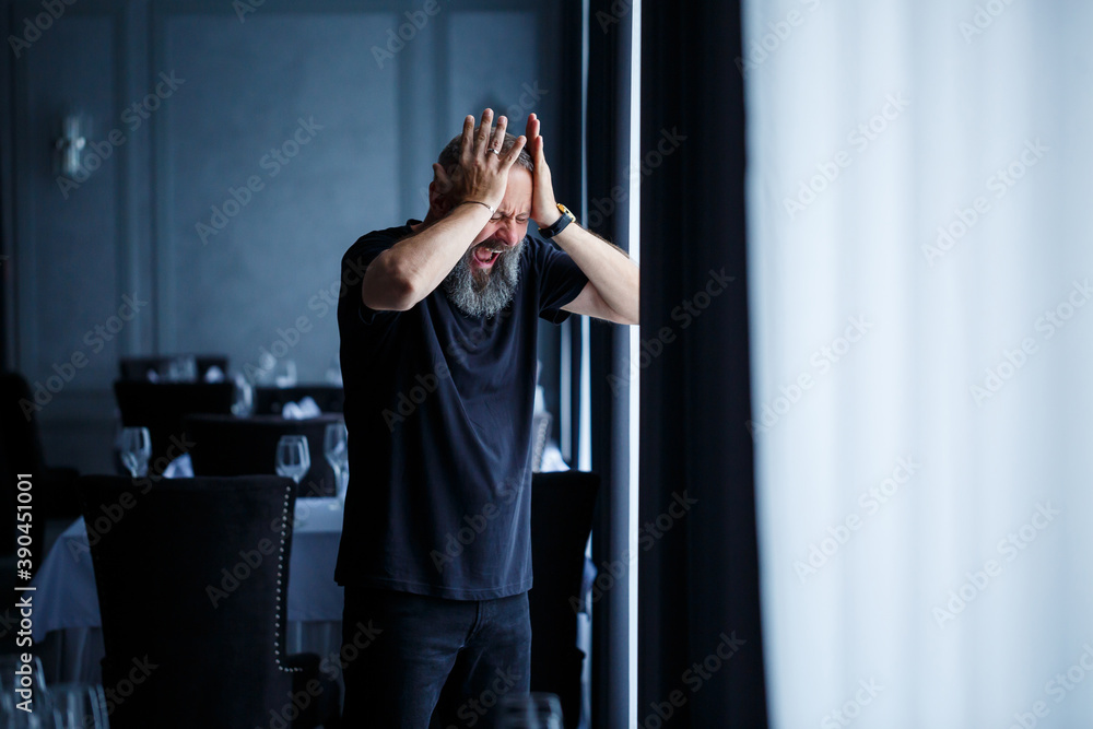 Fototapeta premium Emotional portrait of an adult gray-haired man with a beard in a black t-shirt
