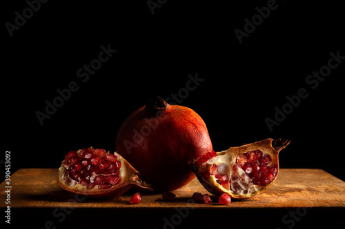 Baroque style still life with a whole pomegranate and two quarters on a wood and dark background. photo