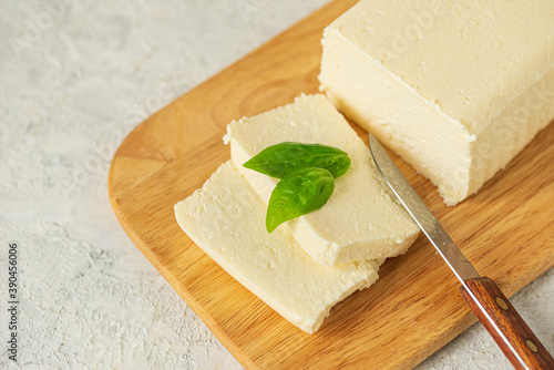 tofu, paneer, soy cheese, curd cheese, brynza, feta, Adyghe cheese with Basil and a knife on a wooden cutting Board on a light background photo