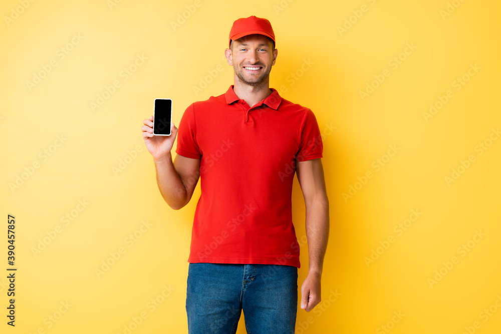 delivery man in red cap holding smartphone with blank screen on yellow