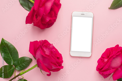 Mobile phone and roses flowers on a pink pastel background photo