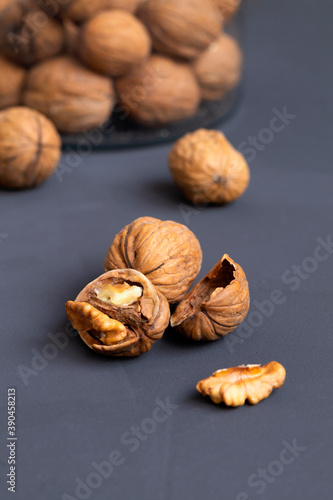 close-up peeled walnuts in shells on a black table and in a glass jar. brown nuts on a dark background. dried walnut and fruit. copy space. vertical