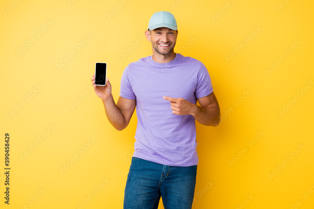 happy man in blue cap pointing with finger at smartphone with blank screen on yellow happy man in blue cap pointing with finger at smartphone with blank screen on yellow
