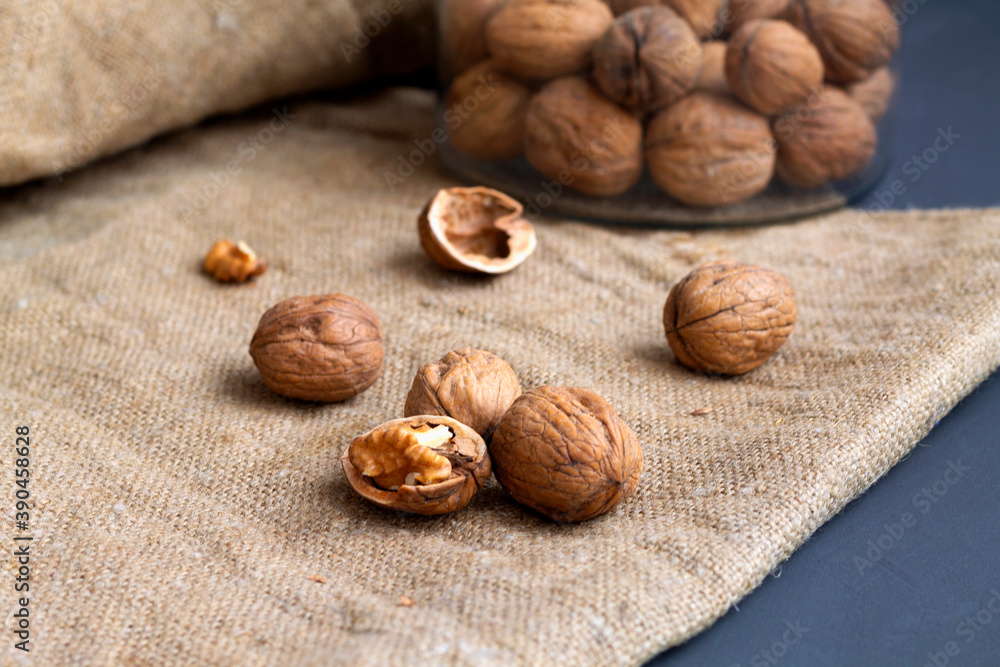 close-up three walnuts. unpeeled and peeled walnuts in shells on a black table and in a glass jar. brown nuts with sackcloth on a dark background. copy space. dried walnut and fruit. close-up three walnuts. unpeeled and peeled walnuts in shells on a black table and in a glass jar. brown nuts with sackcloth on a dark background. copy space. dried walnut and fruit.