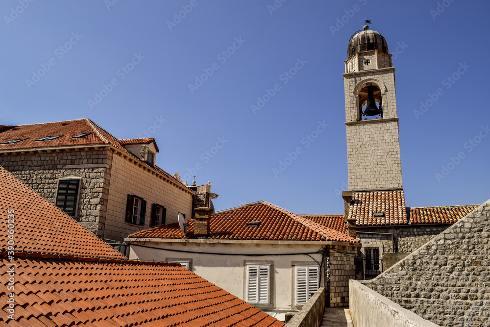 Ceramic tile roofs and a church's tower, in Dubrovnik old city. The day is beautiful and the sky is blue.