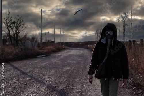 Man in gas mask walks along a rural road against post-apocalyptic landscape. The only survivor after a man-made disaster. Environmental, chemical and toxic pollution of the planet. Concept background