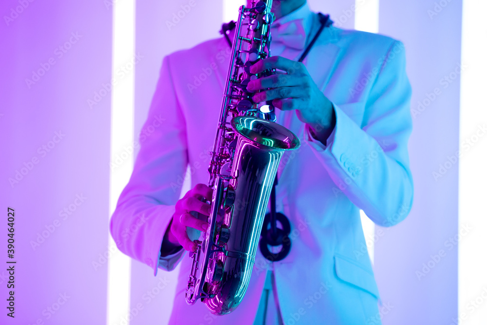Obraz premium Man's hands with saxophone against the background of neon lamps. Fingers playing a saxophone. Close up musical instrument.