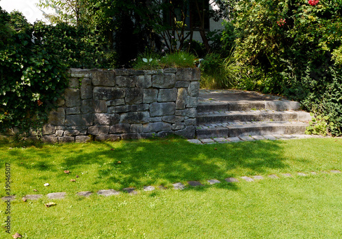 Old stone steps in the park. Lawn and trees. Landscaping. Support wall.
