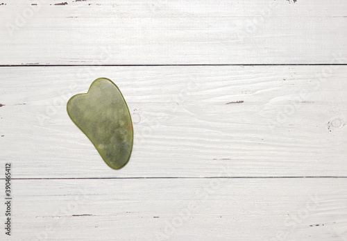 Gouache scraper made of natural green stone on a white wooden background. Anti-aging massage, skin care. Free space for text, top view. photo