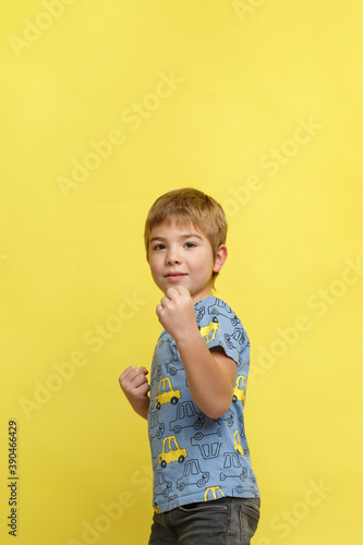 Little emotional boy in casual clothes in a fighting stance isolated on a yellow background.