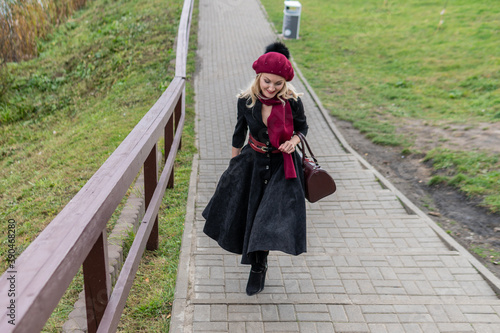 walks up the stairs and in burgundy palla and biret, with beautiful eyes in black clothes, in the fall against the background of trees blue clouds.