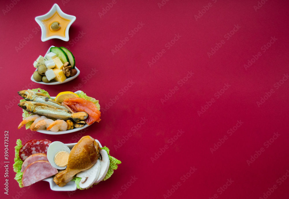 Plate in the form of a Christmas tree with protein food - meat, fish, cheeses, nuts, etc. Red background. The concept of keto diet treats for the holiday. Copy space