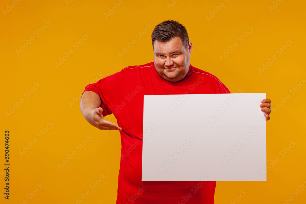 Fat man in red t-shirt displaying a white banner ad isolated over a yellow background. Fat man in red t-shirt displaying a white banner ad isolated over a yellow background.