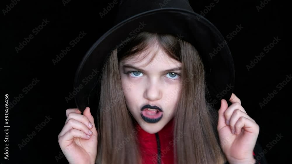 Emotional little / young girl in a witch hat sings a song on a dark background Emotional little / young girl in a witch hat sings a song on a dark background