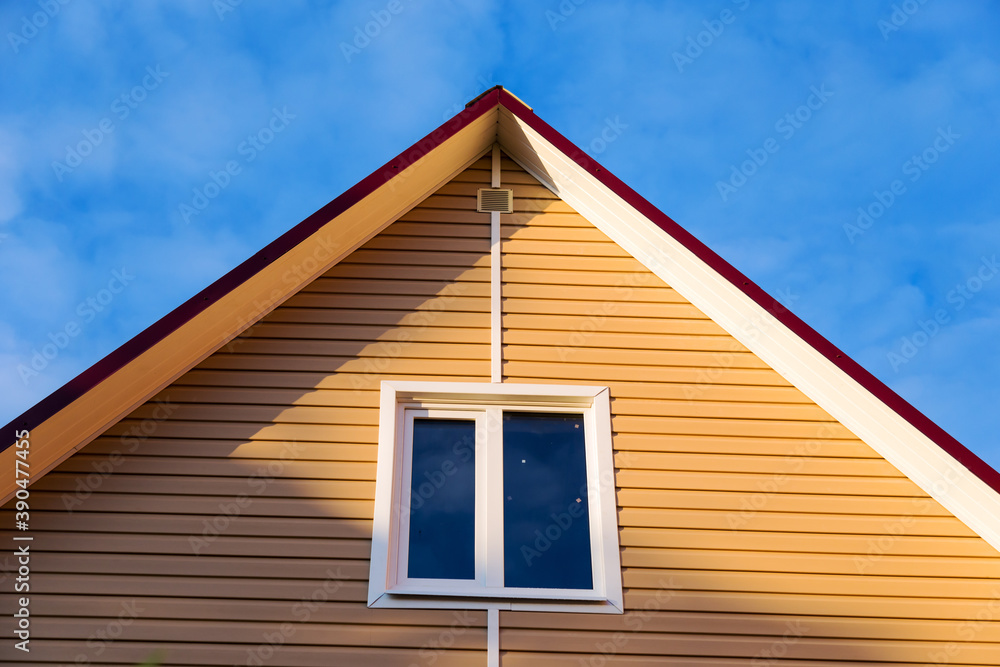 The facade of a new house clad with siding, with windows, against a blue sky, bottom view.