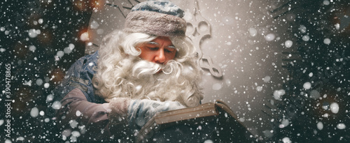 Magical russian Santa Claus (Grandfather Frost) in a blue caftan sits in front of the christmas tree and read large opened wishes book. Panoramic banner. Christmas concept