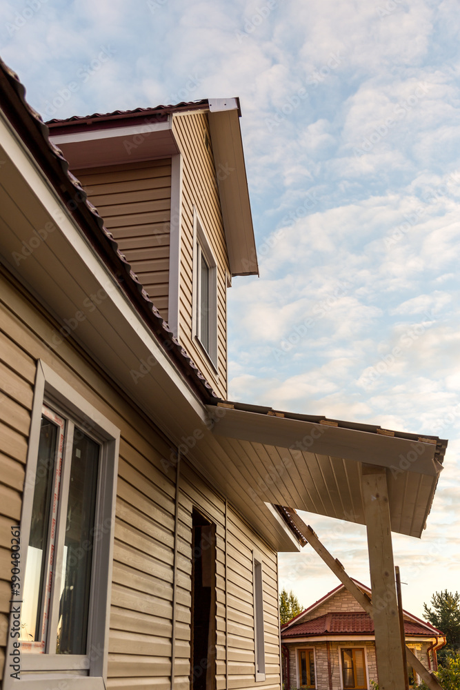 The facade of a new house clad with siding, with windows, against a blue sky, bottom view.