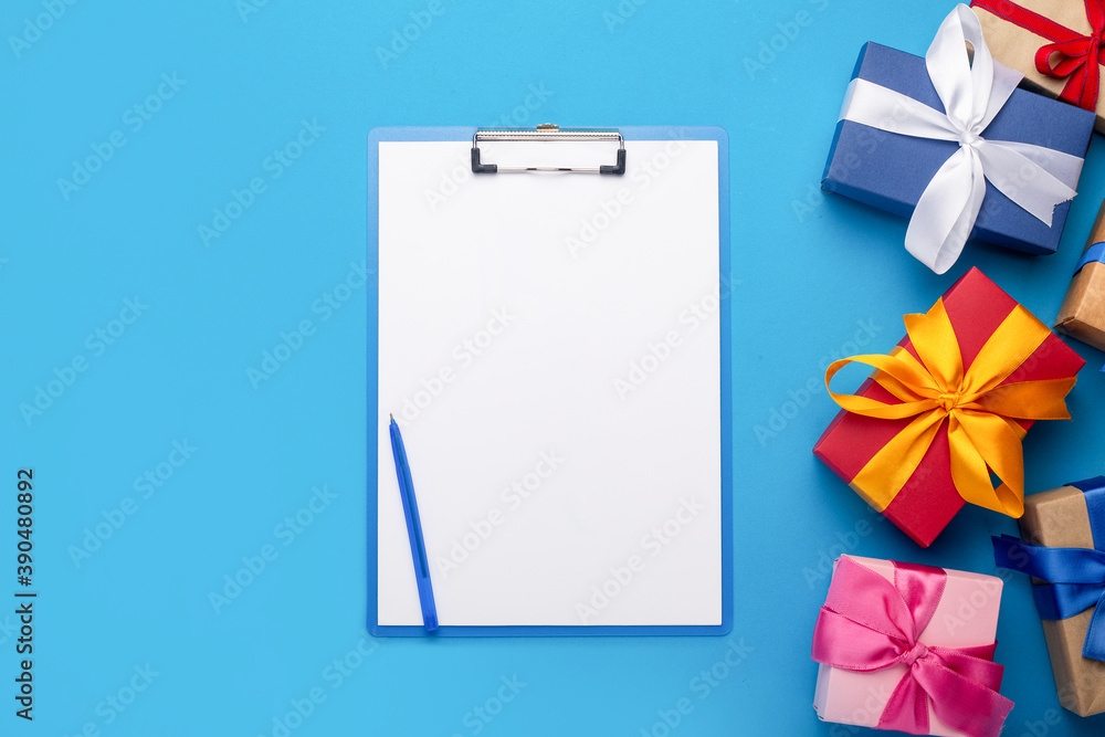Clipboard with a blank sheet and gifts on a blue background. Gift shopping concept Clipboard with a blank sheet and gifts on a blue background. Gift shopping concept
