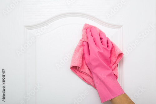 Woman hand in pink rubber protective glove wiping white wooden door with dry rag. General or regular cleanup. Cleaning service. Closeup.