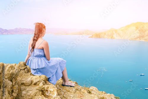 Girl in a blue dress sits on the mountain and admires the seascape. The traveler looks at the mountains and the sea. Hiking, adventure and active tourism © Антон Брехов