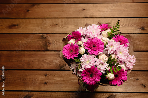 A large beautiful bouquet of chrysanthemums, gerberas, roses and ferns in pink and purple colors wrapped in brown craft paper on a wooden background. Postcard for the holiday. Close-up
