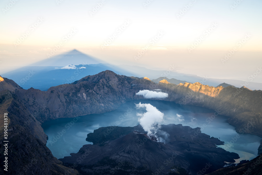 Pink sunrise with triangle shadow of the peak, landscape with clouds in the morning, beautiful volcano Rinjani Gurung at Lombok Island, Indonesia. Small lake in the mountains. 3726m peak Mount Rinjani