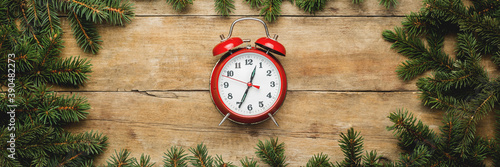 Fototapeta Naklejka Na Ścianę i Meble -  Red vintage alarm clock on a wooden background with Christmas tree branches. Christmas, Christmas morning. Banner