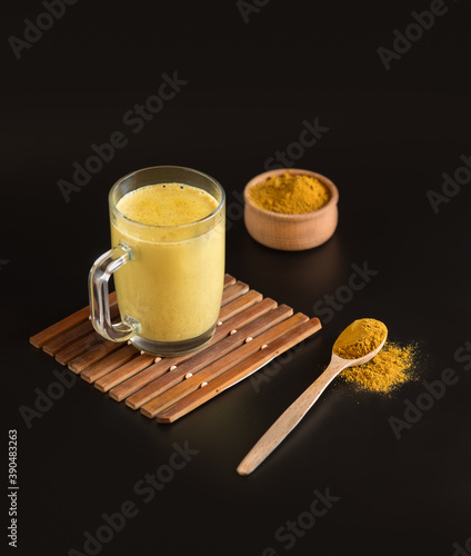 Glass Cup with healthy Indian drink Golden milk-turmeric latte mixed with cardamom, ginger, cinnamon, allspice on black background. Vertical frame