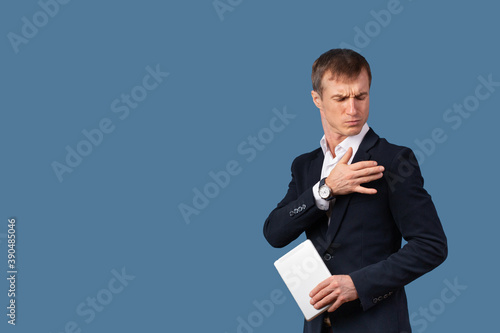 An arrogant male businessman in a suit shakes the dust off his clothes and shoulder with contempt. Studio shot on a blue background. photo