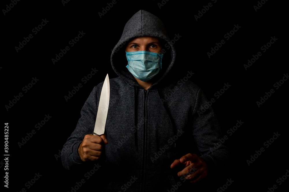 Young man in medical mask points finger while holding knife on black background. Young man in medical mask points finger while holding knife on black background.