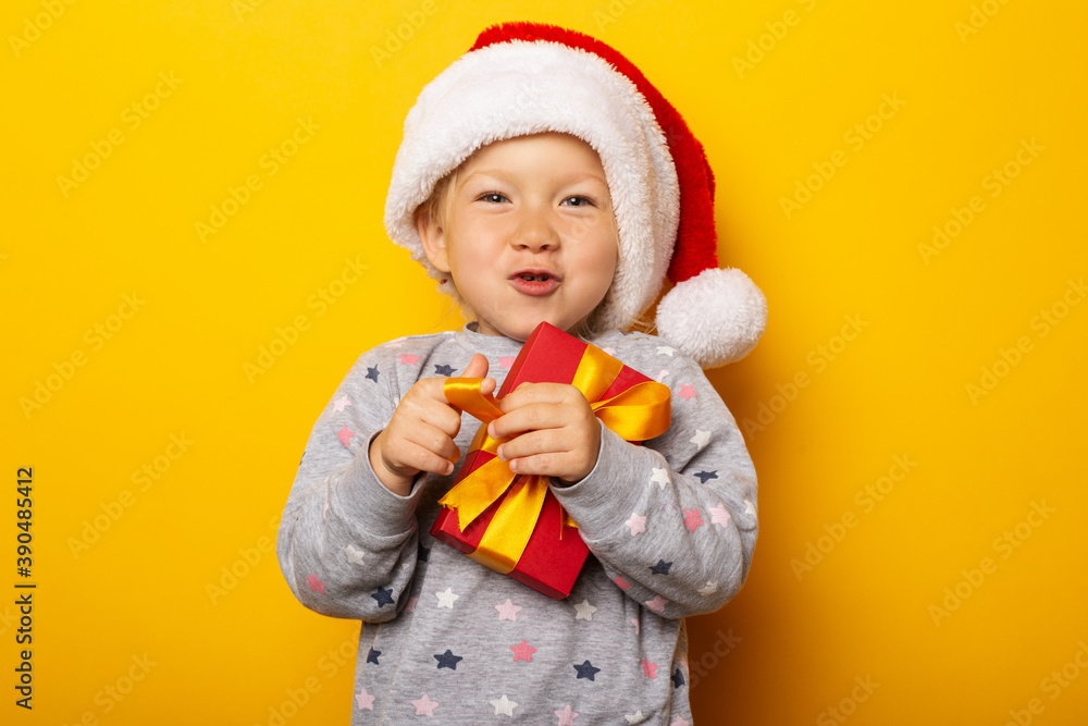 Child in a Santa Claus hat holds a gift on a yellow background. Gifts for Christmas, Christmas morning. Banner Child in a Santa Claus hat holds a gift on a yellow background. Gifts for Christmas, Christmas morning. Banner