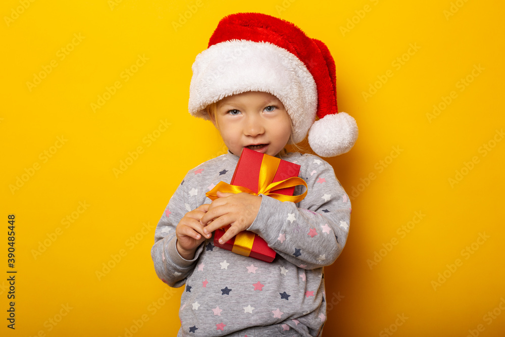 Child in a Christmas hat holds a gift on a yellow background. Gifts for Christmas, Christmas morning