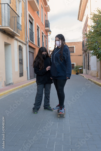 A girl holds another girl while she learns to skateboard.