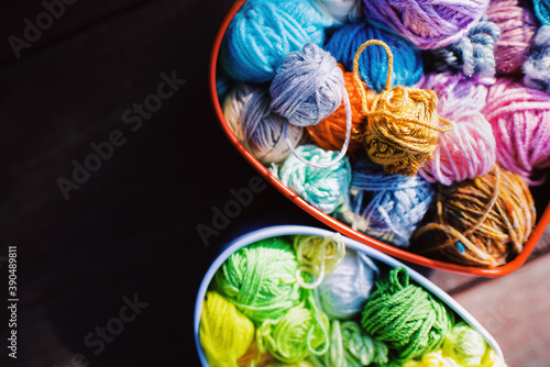 Heart-shaped boxes with multi-colored skeins of yarn for knitting on wooden background in the garden on spring day. Crochet and knitting. Women's working space. 