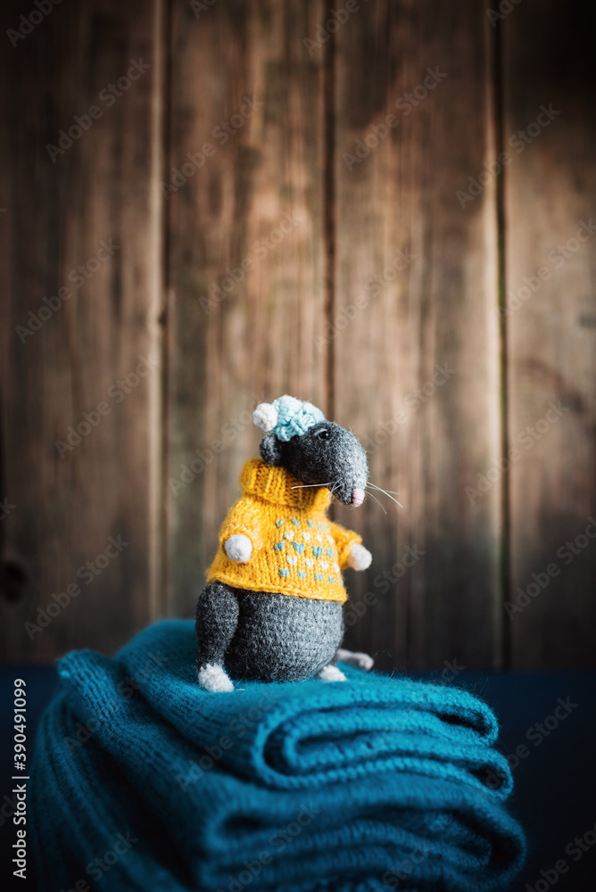 Fototapeta premium Handmade knitted toy. Amigurumi black rat toy in blue hat and yellow sweater on the blue and wooden background . Crochet stuffed animals.