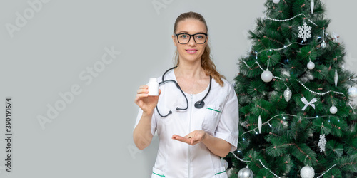 Banner. Female doctor holds pills in background of Christmas tree. Treatment of digestion from overeating during holidays and new year. First aid at home. Online recommendation for taking medications.