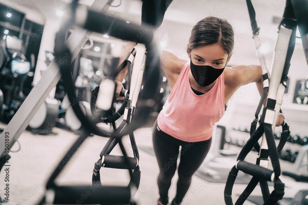 Fototapeta premium Woman training at gym wearing face mask for Coronavirus prevention while exercising strength indoors.