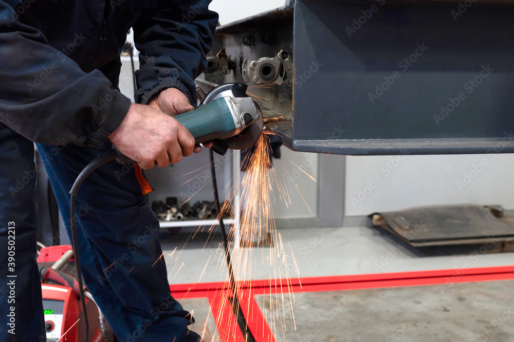 A welder welds and assembles a truck trailer part in a garage. Service of trailers and cars.