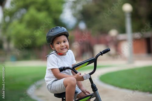 A healthy young boy sitting on his bike on a park trail who is wearing a safety helmet, t-shirt and shorts.